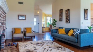 Uma sala de estar com um sofá azul, duas poltronas, um tapete estampado e uma parede de tijolos.