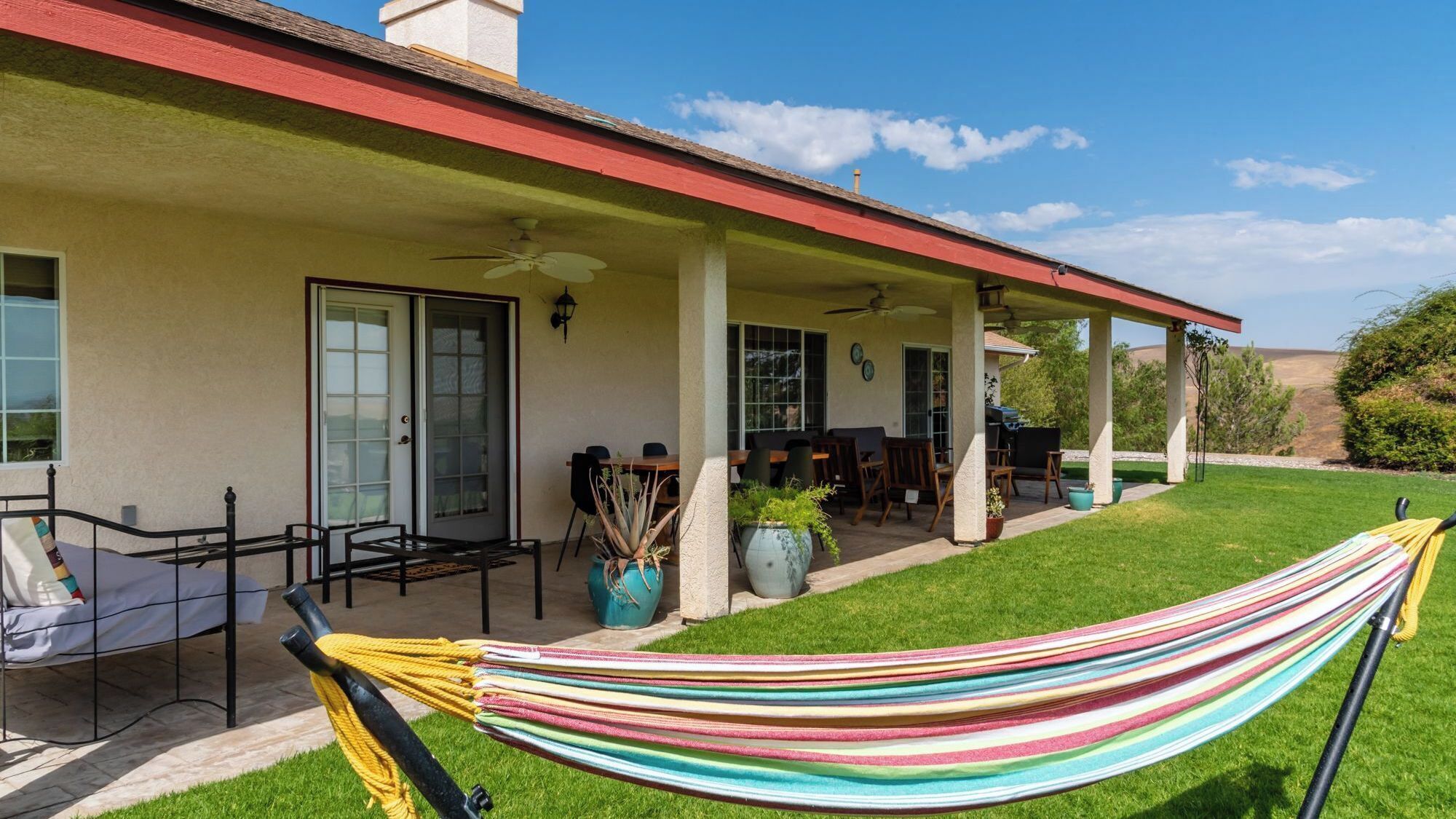 Un patio cubierto con mobiliario exterior, una hamaca y vistas del paisaje circundante.