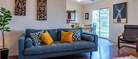 A living room with a blue sofa, a wooden floor, and artwork on the walls.