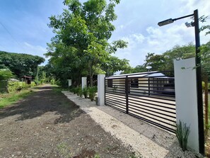 A gated entrance with a gravel path leading to a building, surrounded by greenery and a clear sky. - Gorgeous Costa Rican Villa surrounded by nature. (Coyolar)