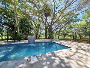 A rectangular swimming pool with a stone waterfall feature, surrounded by trees and a concrete deck. - Gorgeous Costa Rican Villa surrounded by nature. (Coyolar)
