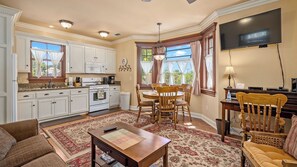 A well-lit kitchen with white cabinets, a dining area with a wooden table and chairs, a living room with a sofa and a TV, and a large window with curtains. - Lewis Loft by Avantstay Two Suites + Walk to Town Paso Robles (Paso Robles)