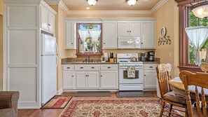 A kitchen with white cabinetry, a stove, a microwave, and a dining area with a wooden chair. - Lewis Loft by Avantstay Two Suites + Walk to Town Paso Robles (Paso Robles)