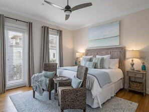 A bedroom with a bed, two chairs, a small table, a ceiling fan, and a nightstand with a lamp. - Amazing Rooftop Views | 2 Min Walk to Beach (Santa Rosa Beach)