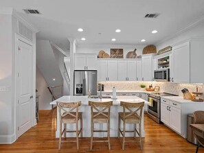 A modern kitchen with white cabinetry, a central island with bar stools, stainless steel appliances, and a wooden floor. - Amazing Rooftop Views | 2 Min Walk to Beach (Santa Rosa Beach)