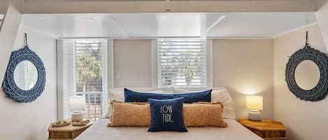 A bedroom with a bunk bed, a large bed with a blue throw, two bedside tables with lamps, and a circular mirror on the wall.