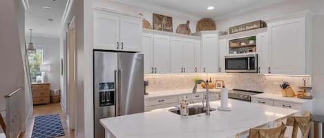 A modern kitchen with white cabinetry, stainless steel appliances, and a central island with bar stools.