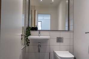 Ein Badezimmer mit einem weißen Waschbecken, einer Toilette und einem Spiegel, der den Raum widerspiegelt.