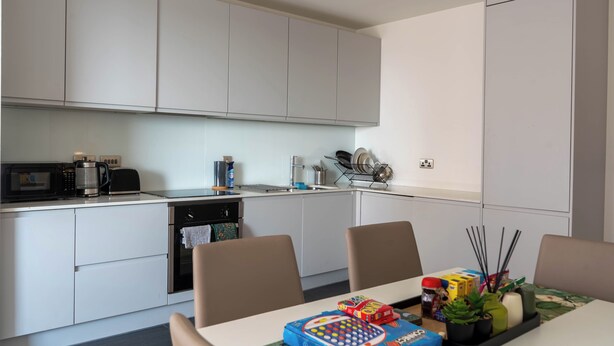 A modern kitchen with white cabinets, a microwave, a coffee maker, and a dining area with a table and chairs. - Morden stay minutes from Manchester City centre (Manchester)