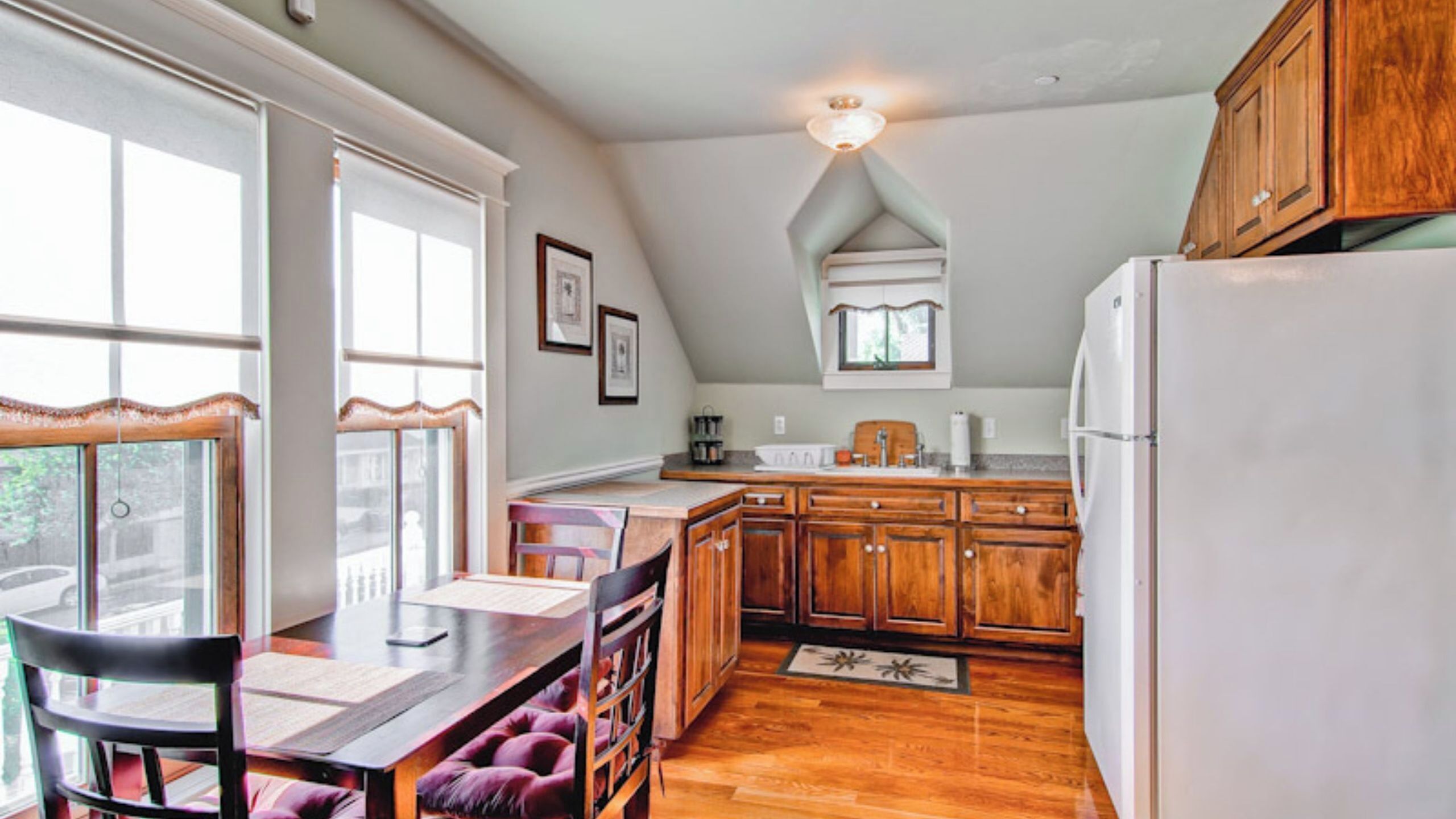 A kitchen with wooden cabinets, a white refrigerator, a dining table with chairs, and a window with curtains.