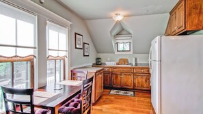 A kitchen with wooden cabinets, a white refrigerator, a dining table with chairs, and a window with curtains.