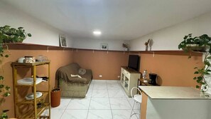 A compact living space with a sofa, a small table, a television, and a shelf with dishes. - House 4 in the Anglo-Brazilian Village (São Paulo)