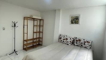 Quarto com cama, um cabideiro, guarda-roupa e um quadro na parede.