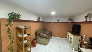 A compact living space with a sofa, a television, a small table, and a shelf unit. - House 4 in the Anglo-Brazilian Village (São Paulo)