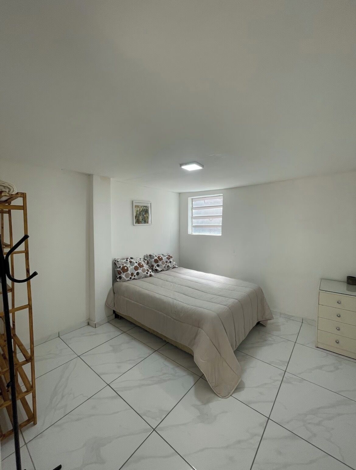 Quarto com uma cama, janela, radiador e cómoda.