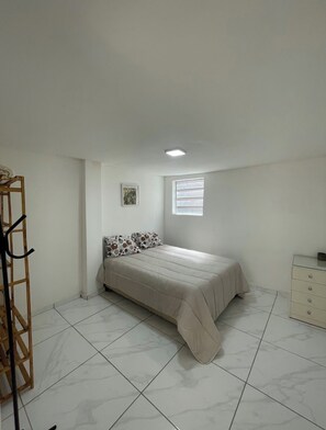 Een slaapkamer met een bed, een raam, een radiator en een dressoir.