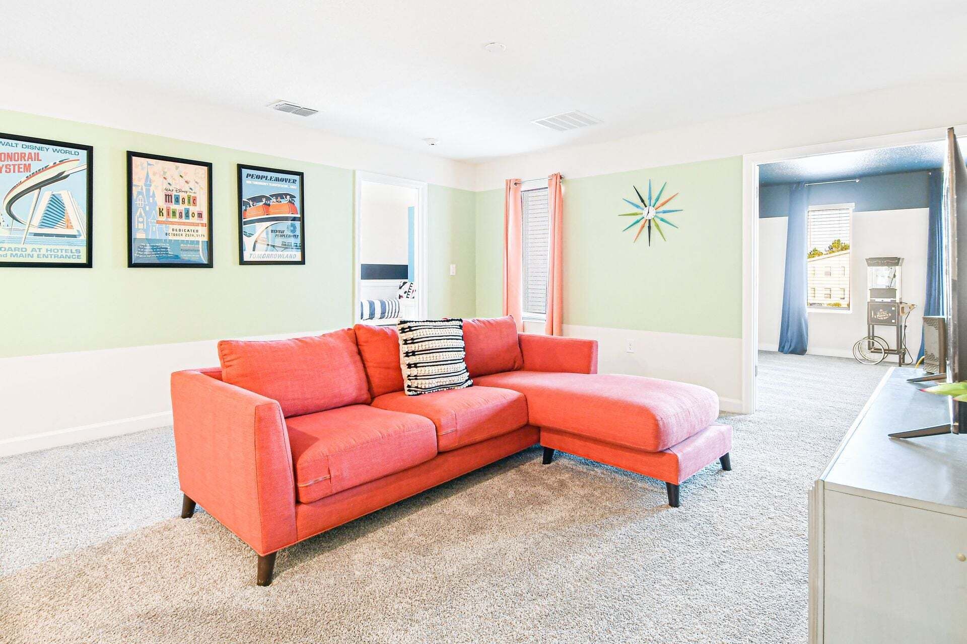 A living room with a red sectional sofa, a small white cabinet, and a wall with framed posters.