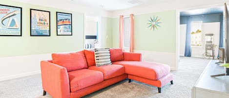 A living room with a red sectional sofa, a small white cabinet, and a wall with framed posters.