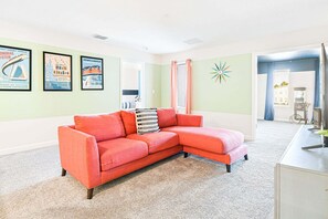 A living room with a red sectional sofa, a small white cabinet, and a wall with framed posters. - Storey Lake Resort Villa | Pool & Resort Fun (Kissimmee)