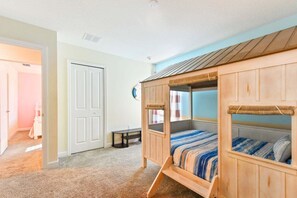 A bedroom with a bunk bed, carpeted floor, and a door leading to another room.