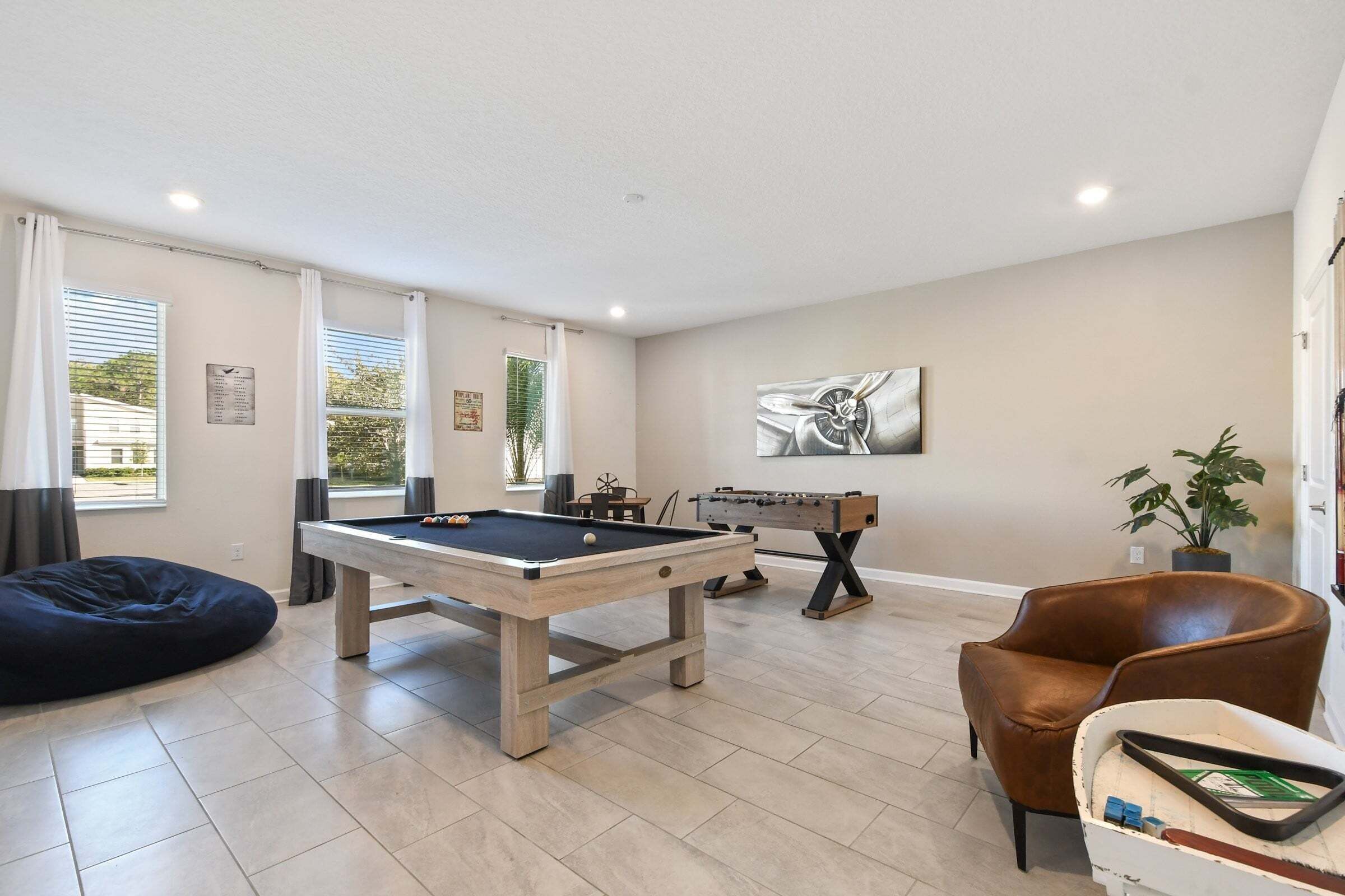 A room with a pool table, foosball table, and a brown leather chair.