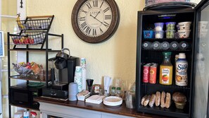 A kitchen counter with a coffee machine, a clock, and a refrigerator stocked with beverages and food items.
