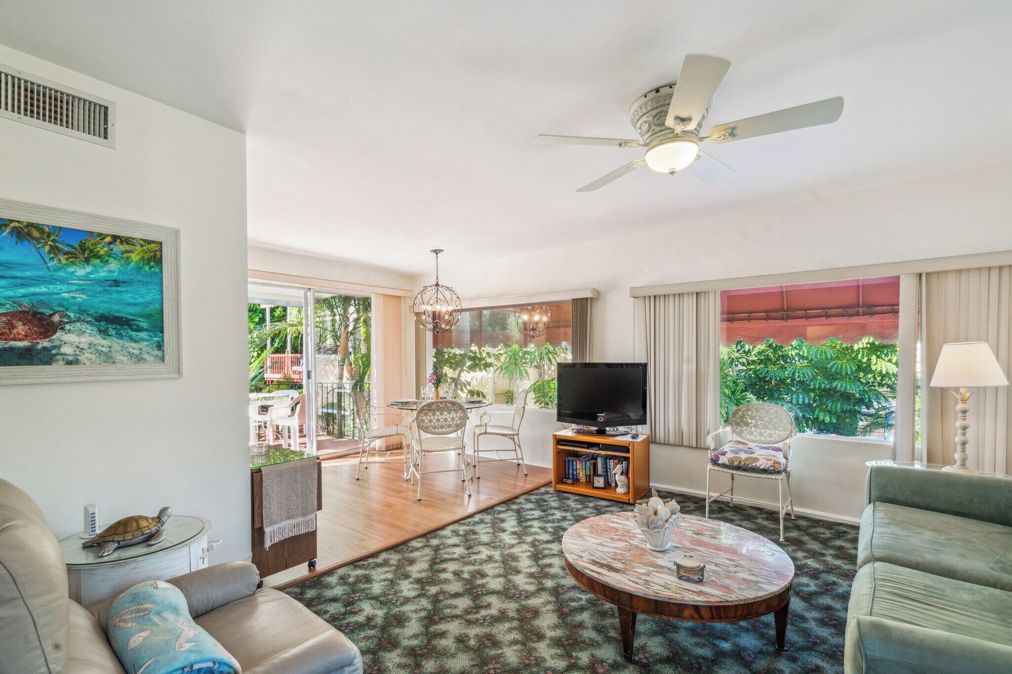 A living room with a ceiling fan, a television, and a dining area with chairs and a table.