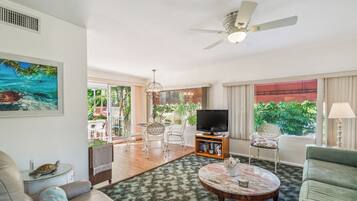 A living room with a ceiling fan, a television, and a dining area with chairs and a table.