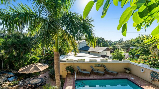 Un patio trasero con piscina, sillas de descanso, una mesa con sillas y un pequeño jardín.
