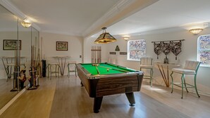 Una mesa de billar en una habitación con piso de madera, un portaobjetos para billar y una lámpara colgante.