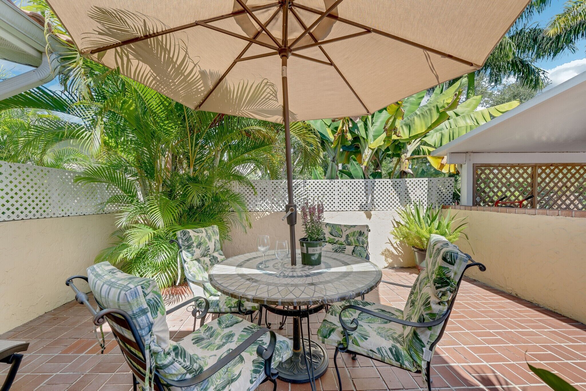 Een terras met een ronde tafel, vier stoelen en een grote parasol.