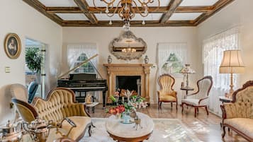 Un salón espacioso con un piano de cola, elegantes sillas, una araña y una chimenea.