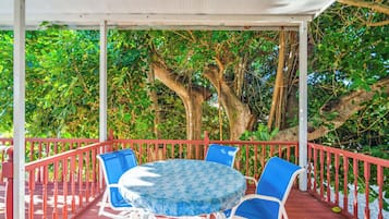 Un patio exterior con una mesa redonda y sillas azules, rodeado por una barandilla roja y árboles.
