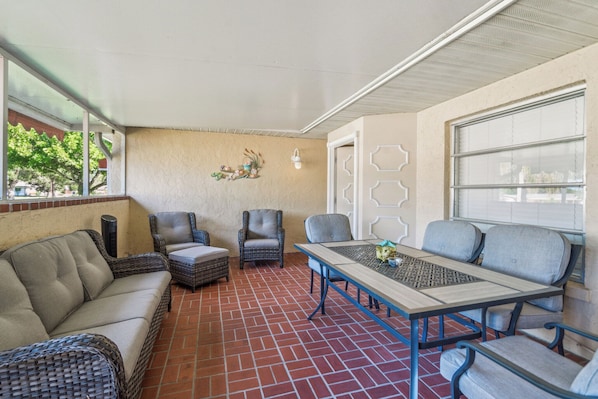 Un patio techado con mobiliario de mimbre, una mesa y un aplique de pared.