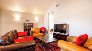 Ein Wohnzimmer mit Ledersofas, einem Couchtisch, einem Fernseher und einem Bücherregal.