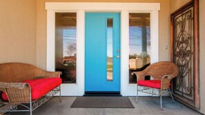 A front entrance with a blue door, two wicker chairs with red cushions, and a metal gate. - Charm on Chestnut by Avantstay Single-level + Fenced Yard + Gas BBQ Walk to Downtown Paso Robles (Paso Robles)