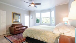 Ein Schlafzimmer mit einem Bett, einem braunen Ledersofa, einem Deckenventilator und einem großen Fenster.