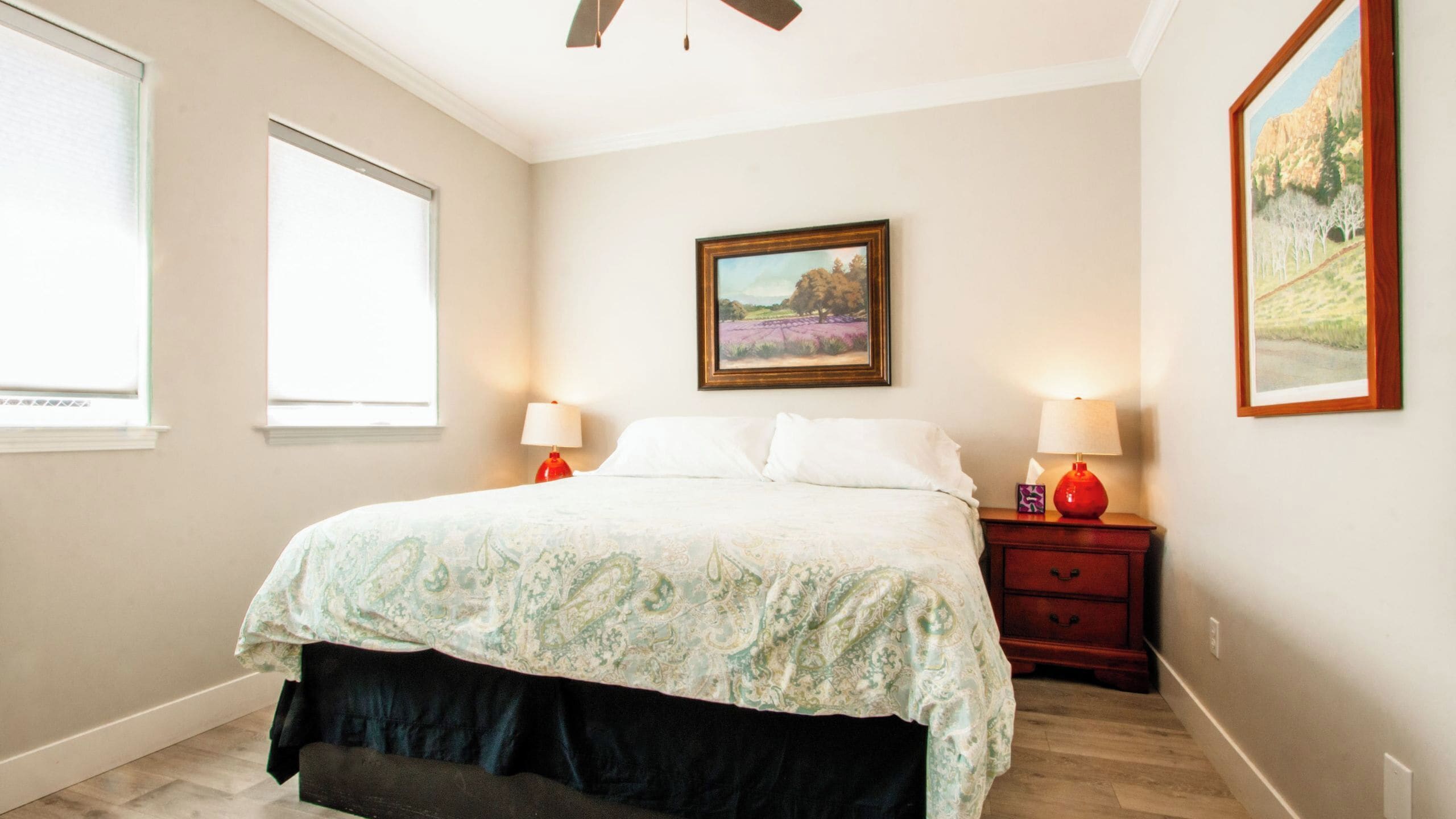A bedroom with a bed, two bedside tables with lamps, a window, and a painting on the wall.