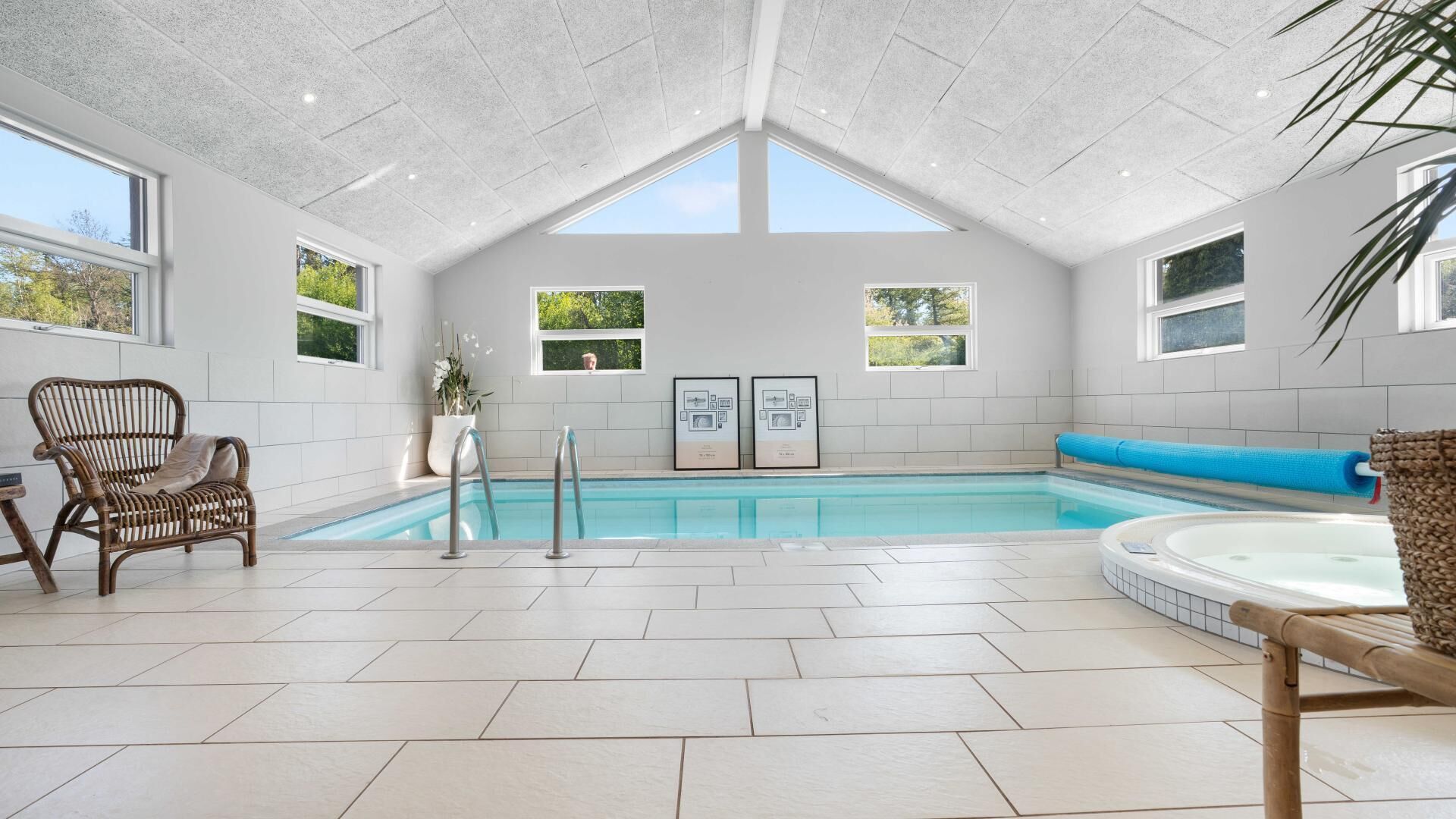 Una piscina interior moderna amb sostre alt, finestres clares i vistes a verdura a l'exterior.