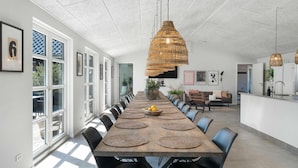 Un comedor amplio con una larga mesa de madera, varias sillas y lámparas colgantes tejidas.