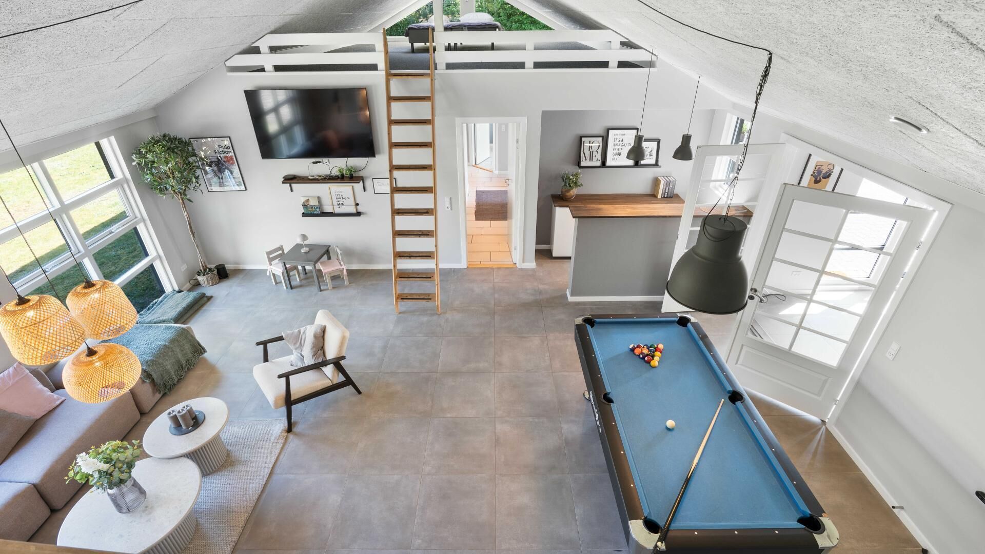 A spacious living area with a pool table, seating, a TV, and a loft bedroom accessible by a ladder.