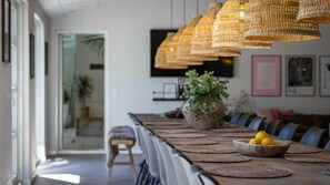 Ein Essbereich mit einem langen Tisch, gewobenen Pendelleuchten und einem Blumentopf.
