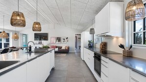 Una cocina moderna con una isla central, iluminación colgante y vistas al área de estar.