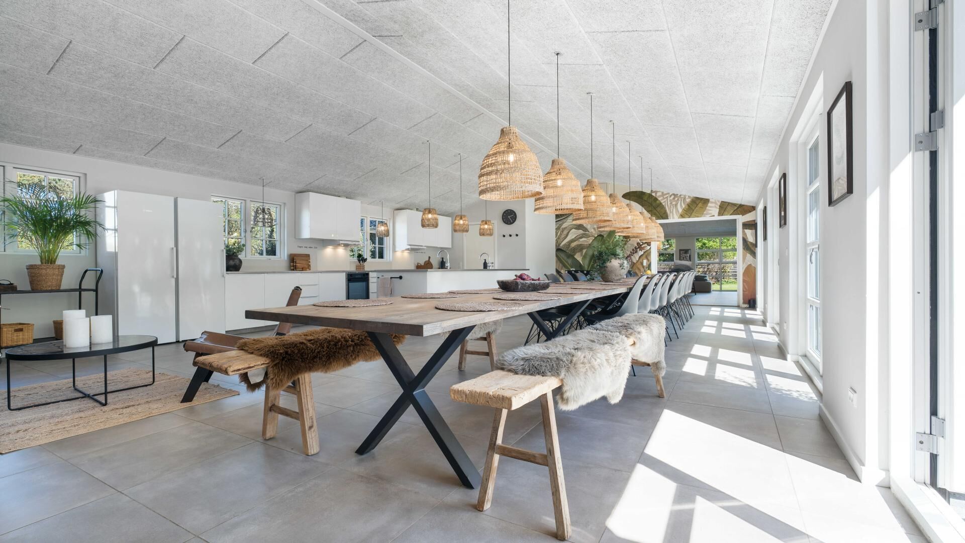 A modern kitchen with a large dining table, pendant lights, and a view to the outside.