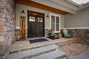 A stone exterior with a wooden welcome sign, a dark front door, and a porch with Adirondack chairs. - Heavenly Haven - Lake Nottely | Double Decker Dock | Firepit (Blairsville)
