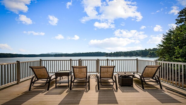 Varanda com quatro cadeiras e uma mesa, com vista para um lago calmo e montanhas ao longe.