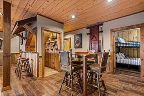 A rustic interior with a wooden ceiling, a dining area with stools, a bunk bed, and a framed raccoon artwork. - Raccoon Ridge - Mountain View | Pet Friendly | Hot Tub | Game Room | Firepit (Blue Ridge)