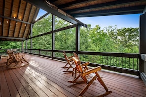 En overdækket terrasse med gyngestole i træ og udsigt til en skov.