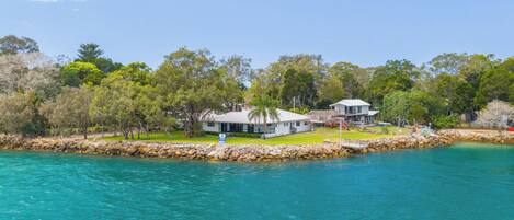 A coastal property with two main buildings, a swimming pool, and a rocky shoreline.