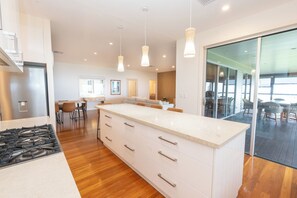 A modern kitchen with a large island, wooden flooring, and pendant lighting. - Sand Bar - Absolute Waterfront Escape, Amity Point (Amity Point)